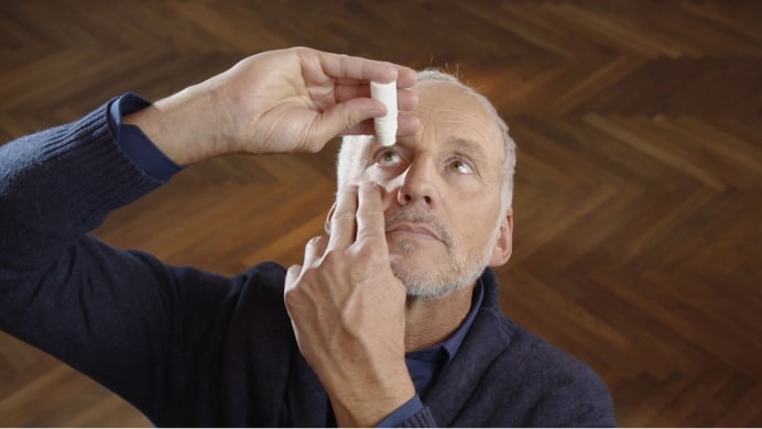 Man pulling back eye-lid to apply drops