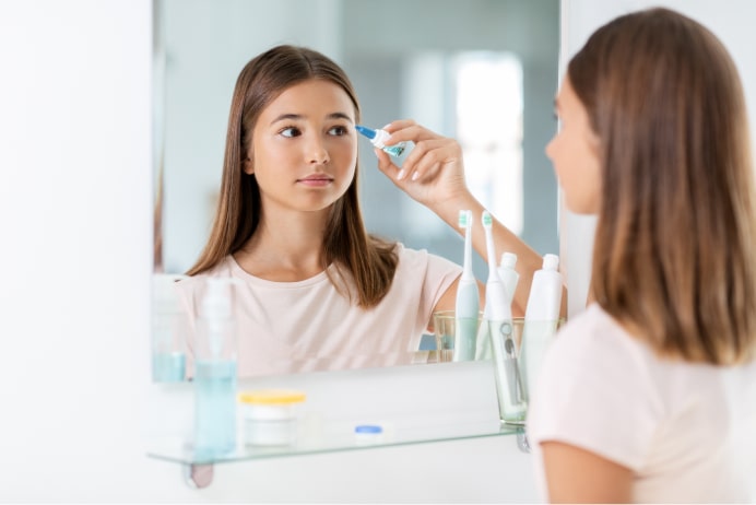 Woman looking in mirror applying eye-drops