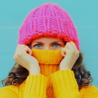 Image shows woman smiling in winter clothes with snow in the background holding giant snowflake in front of her eye.