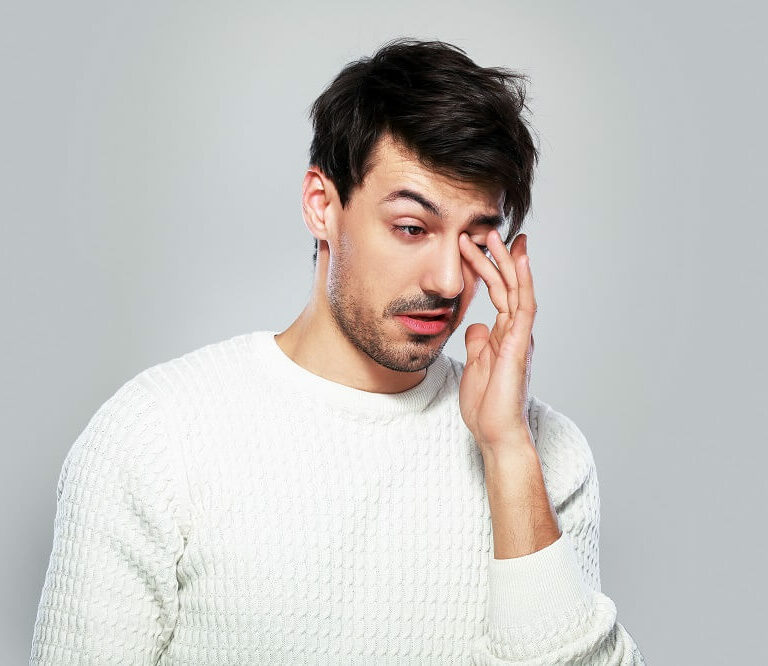 Man in white jumper rubbing watery eye