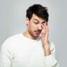 Man in white jumper rubbing watery eye